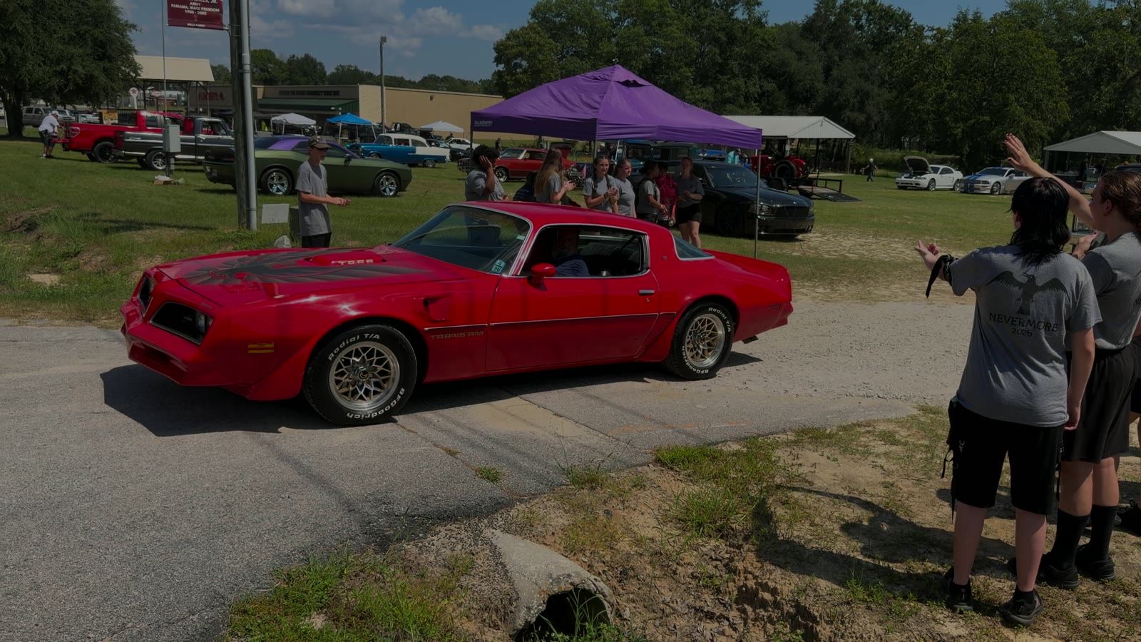 A red Trans Am rolling out past the Pelion band students at the auto show